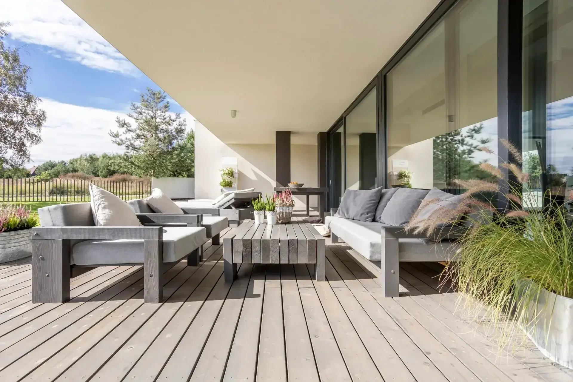 Gezellige loungeplek met houten vlonders onder de overkapping in de tuin, gerealiseerd door Walraven Bouw in Huissen. Wij plaatsen serres, veranda's, overkappingen en buitenverblijven op maat, geheel samen te stellen naar uw eigen smaak en woonwensen.
